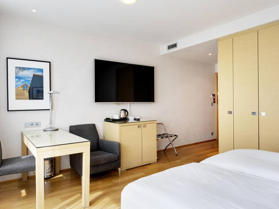 Habitación de hotel con cama, escritorio con silla, televisión, armario y un cuadro en la pared.