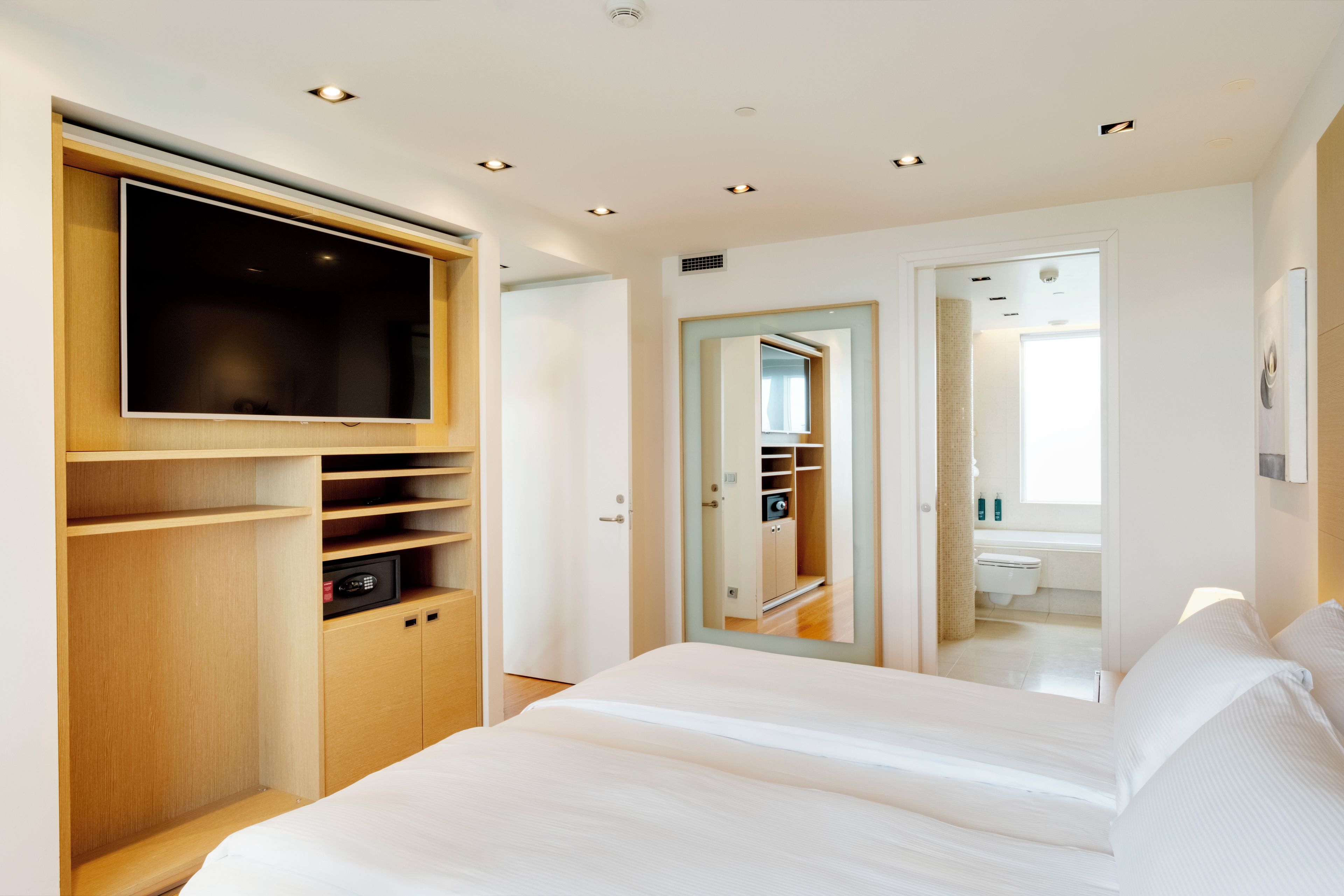Un dormitorio con cama, televisor, armario y baño visible a través de una puerta abierta.