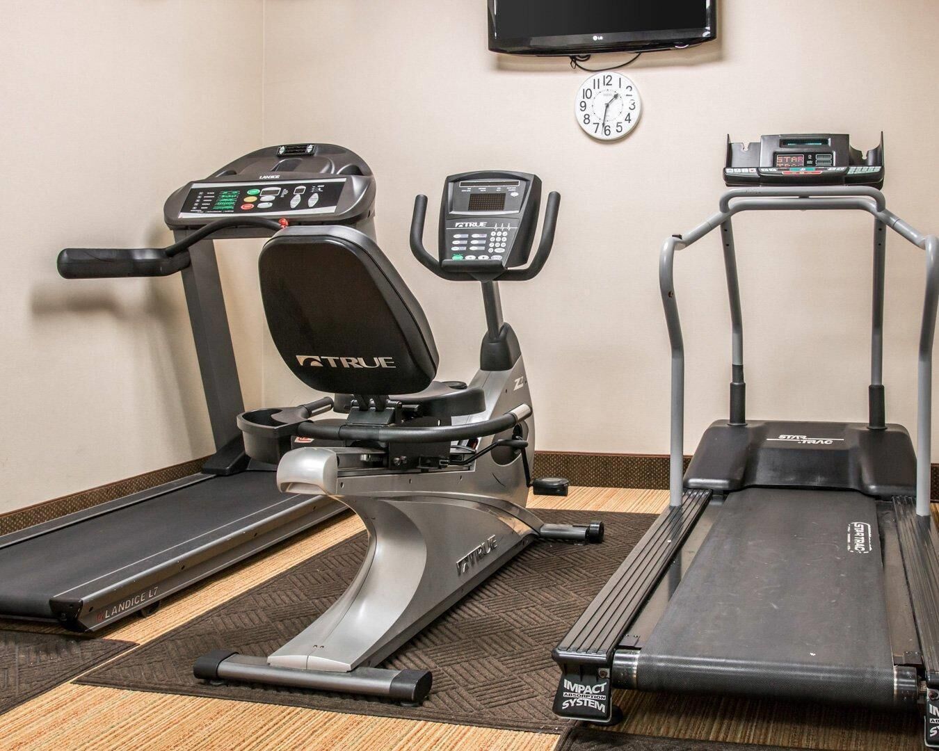 A fitness area with treadmills, a stationary bike, and a wall clock.