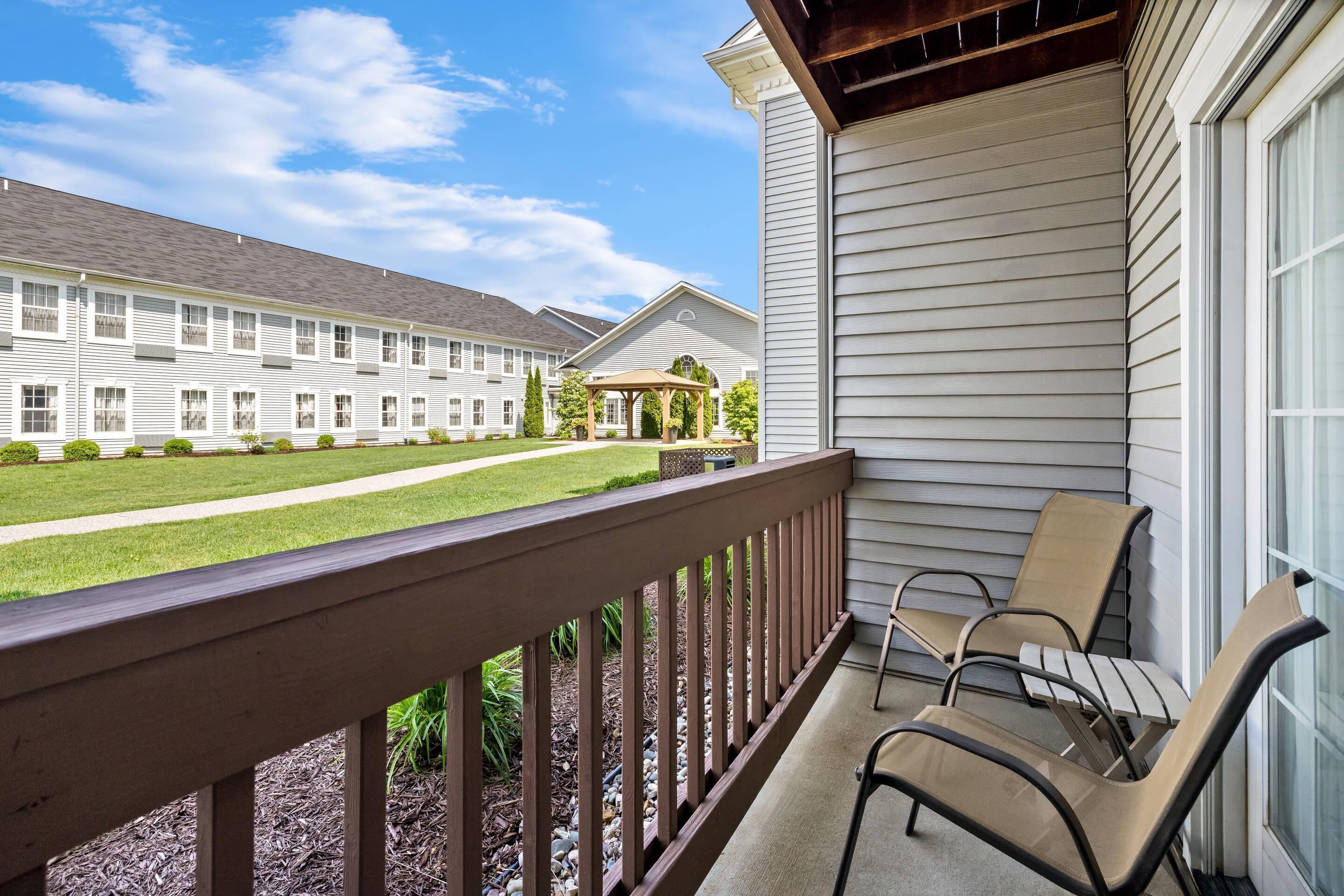 A balcony with a wooden railing, two chairs, and a view of a building with a covered patio.