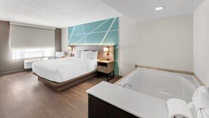 Een hotelkamer met een tweepersoonsbed, een aparte badkamer met ligbad, een bureau en een nachtkastje.
