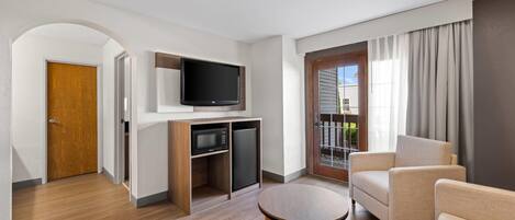 A modern living room with a flat-screen TV, a built-in microwave, a refrigerator, a round coffee table, and a beige sofa.
