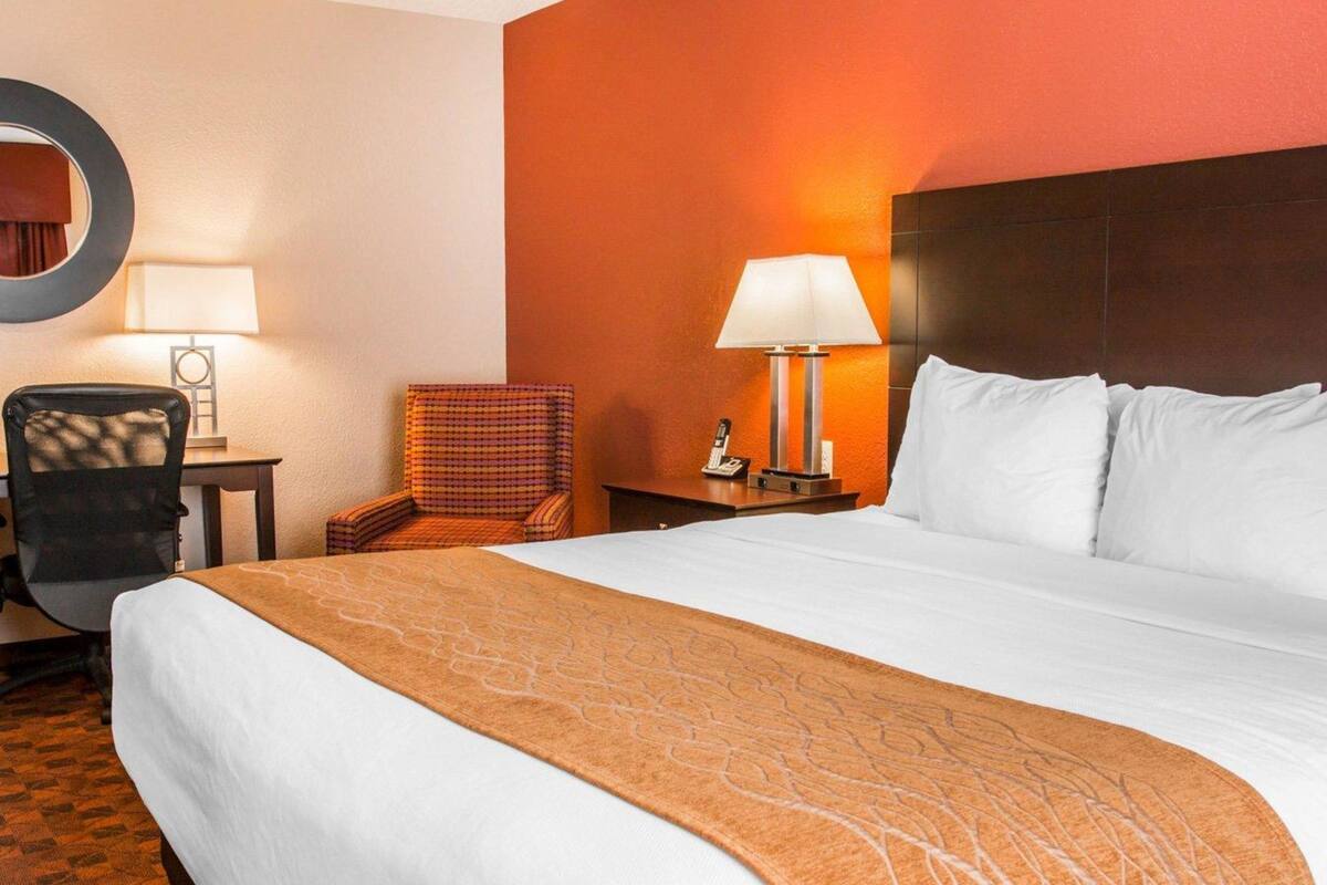 A hotel room with a large bed, a chair, a desk, a lamp, and a phone on the nightstand.