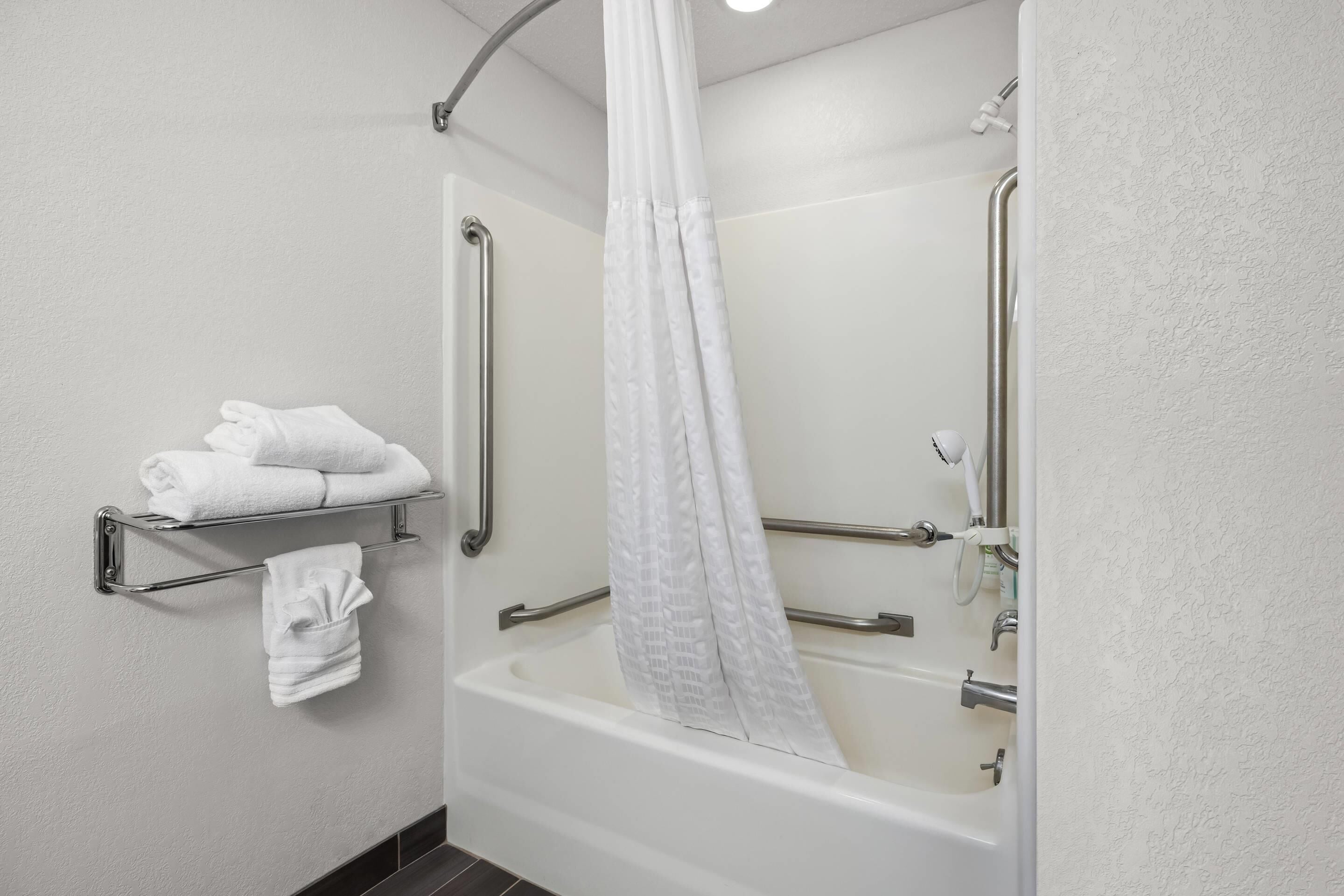A modern bathroom with a bathtub, a shower curtain, a towel rack, and a handrail.