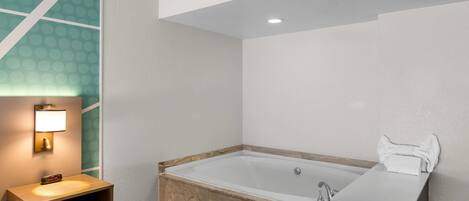 A modern bathroom with a bathtub, a vanity with a mirror, and a nightstand with a lamp.