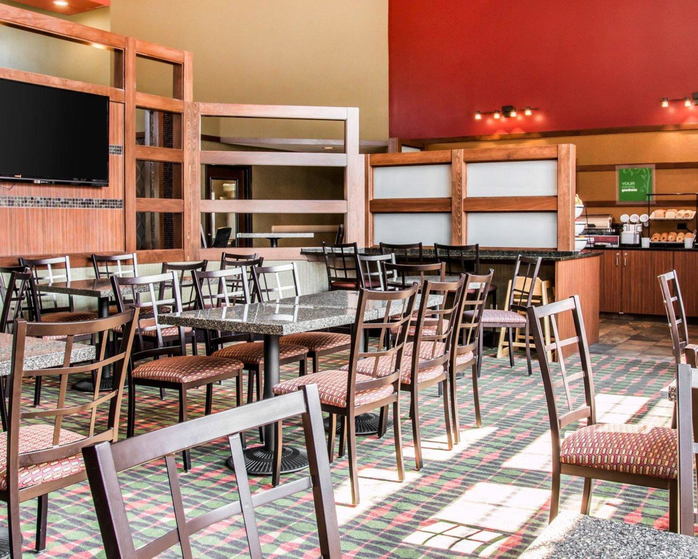 A restaurant with multiple tables and chairs, a television mounted on the wall, and a kitchen area visible in the background.