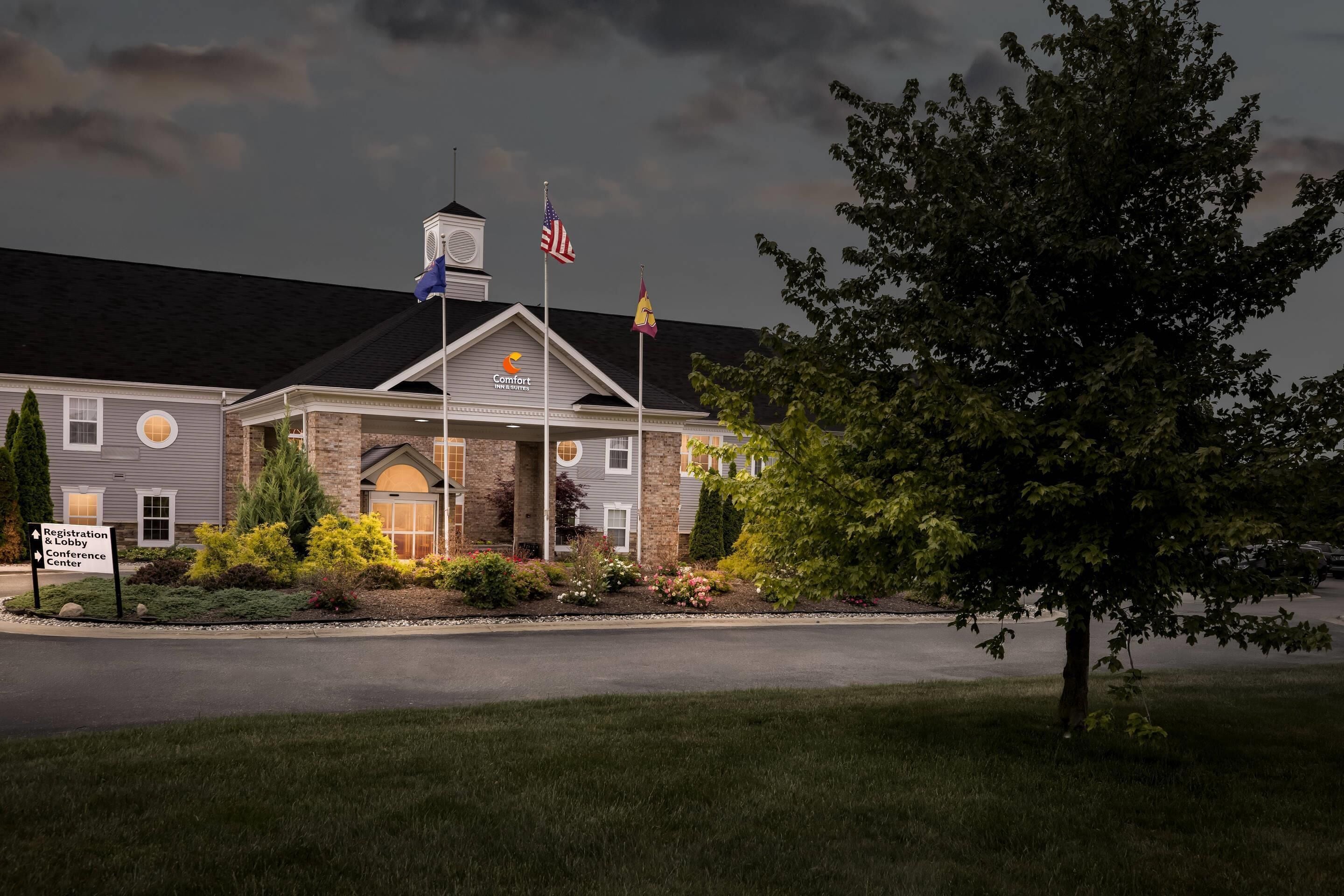 A hotel with a registration and lobby sign, flags, and a well-maintained garden.