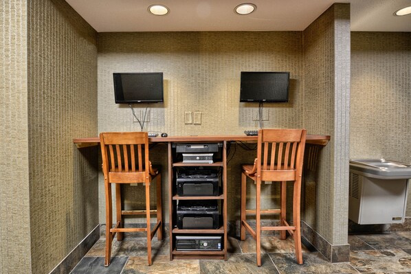 A room with a wooden desk, two chairs, two televisions mounted on the wall, and a sink.