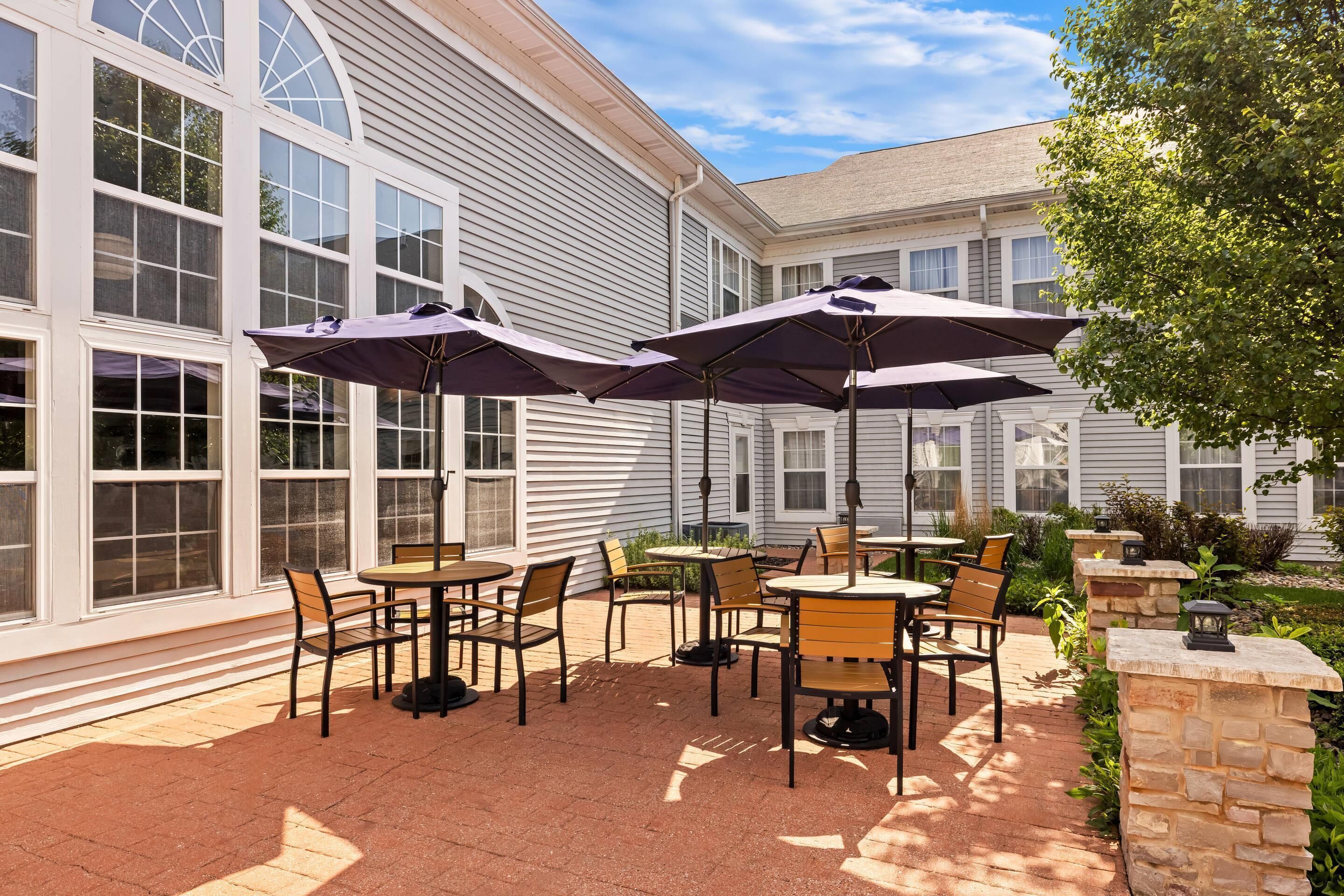 An outdoor patio with tables and chairs, umbrellas, and stone pillars.