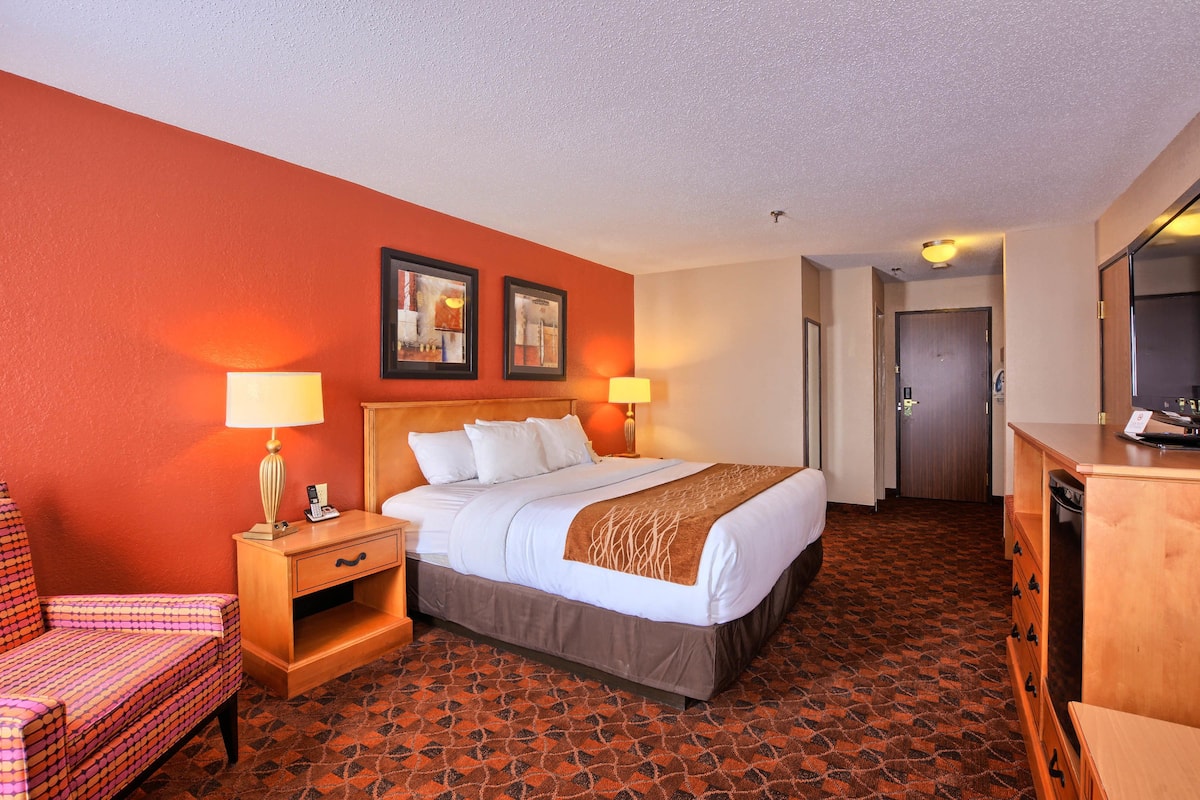 A hotel room with a bed, a desk with a lamp, a chair, and a dresser.