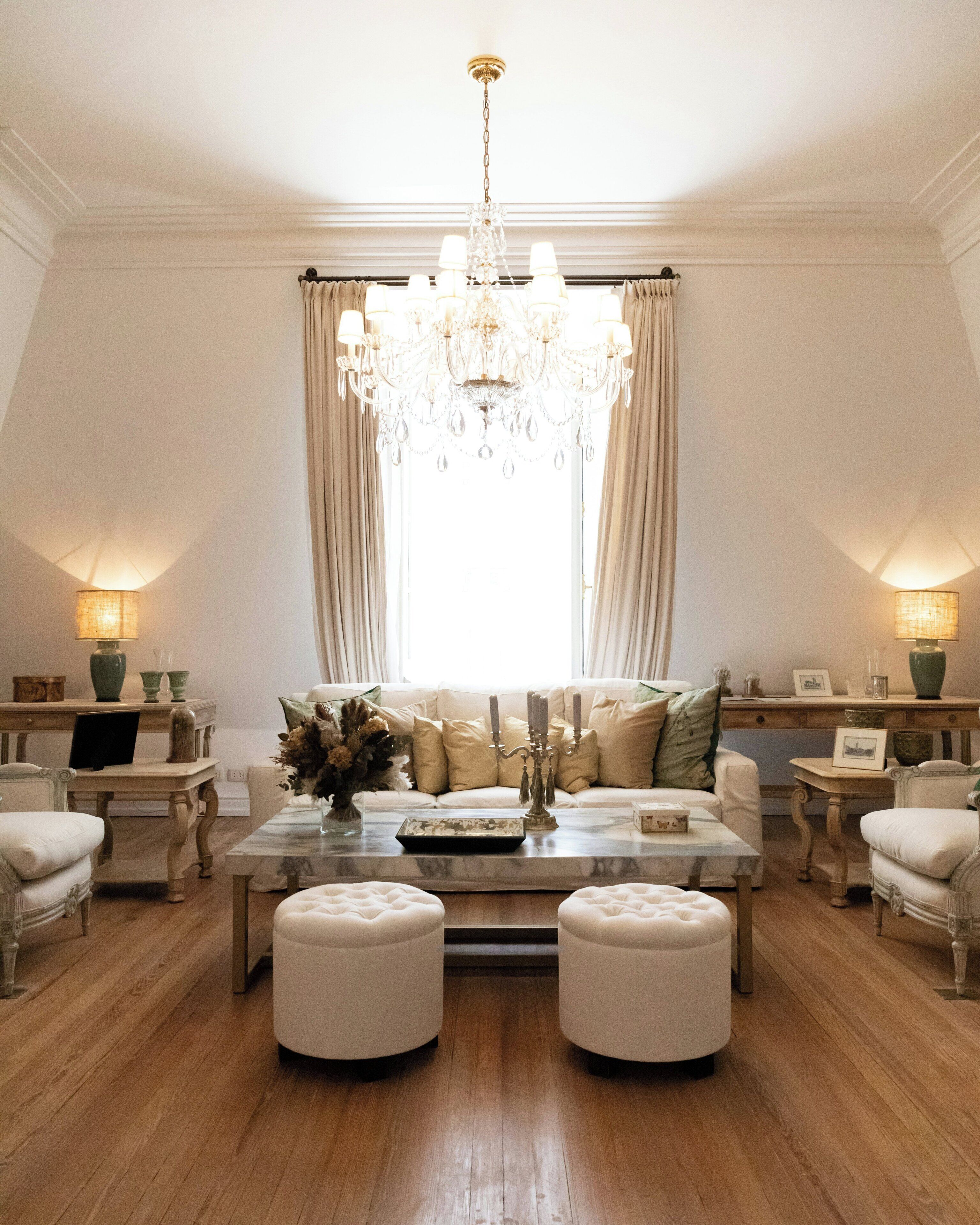 A room with a chandelier, a sofa set, ottomans, a coffee table, and lamps.