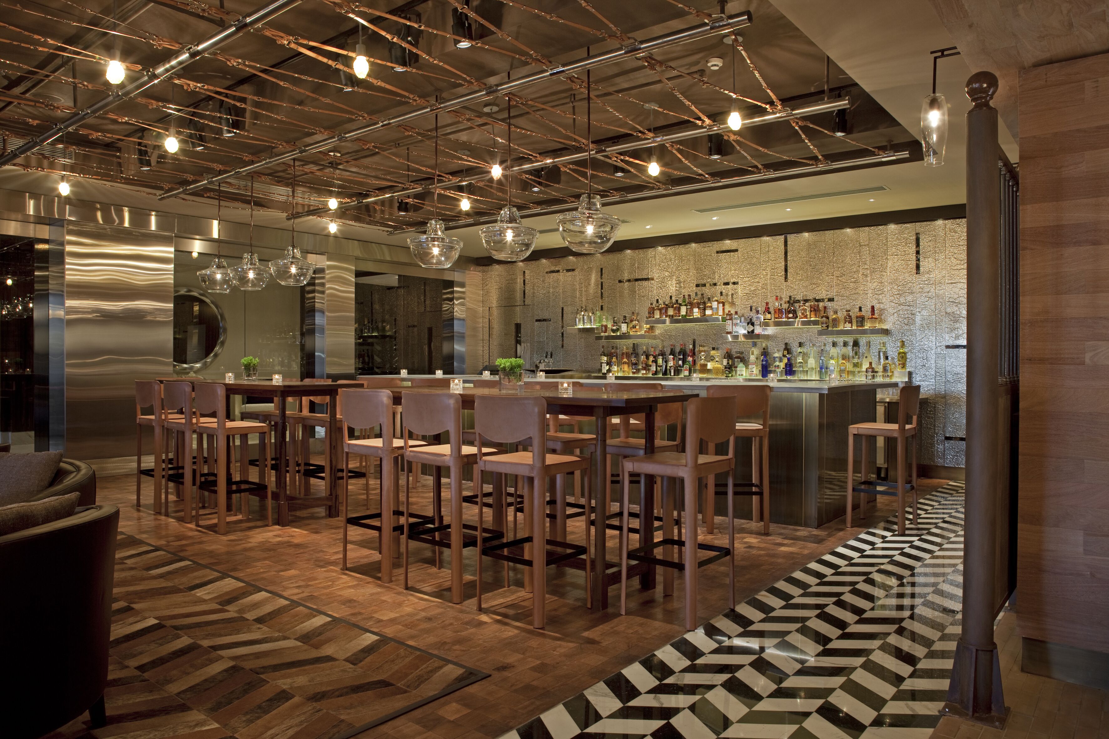 A modern bar area with a bar counter, seating, and a patterned floor.