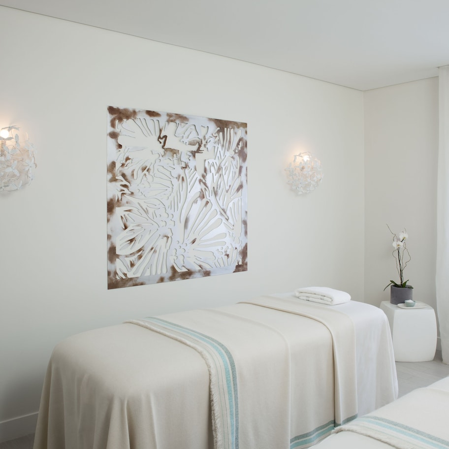 A hotel room with two beds, a wall-mounted artwork, and two wall sconces.