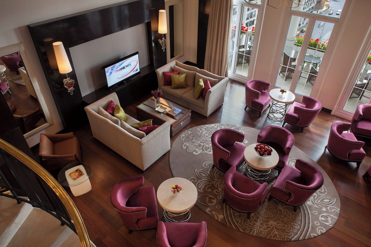 Un moderno hall de hotel con un sofá, sillones, un televisor y vistas a la ciudad.