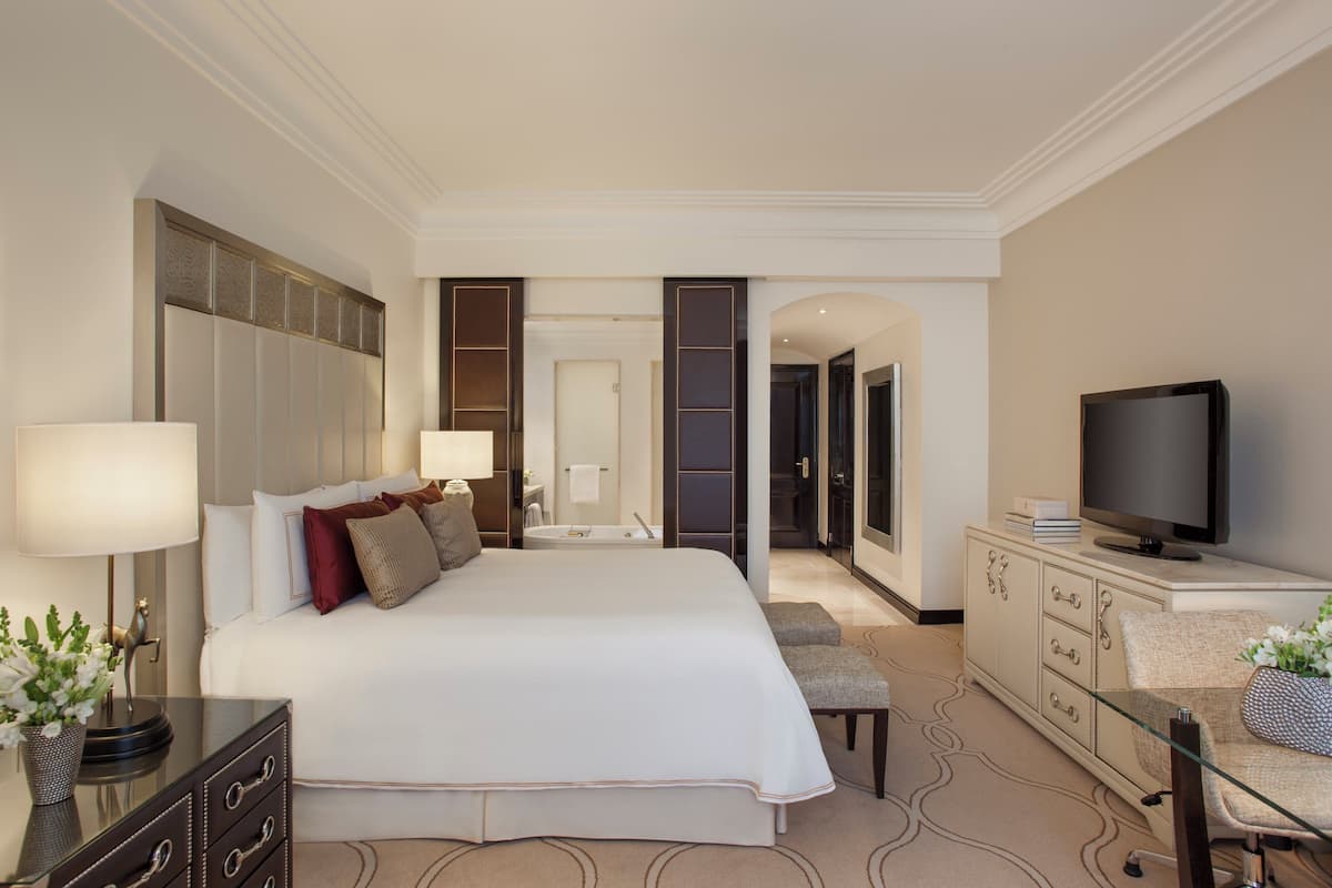 Habitación de hotel con una cama grande, televisión, cómoda y baño visible a través de una puerta abierta.