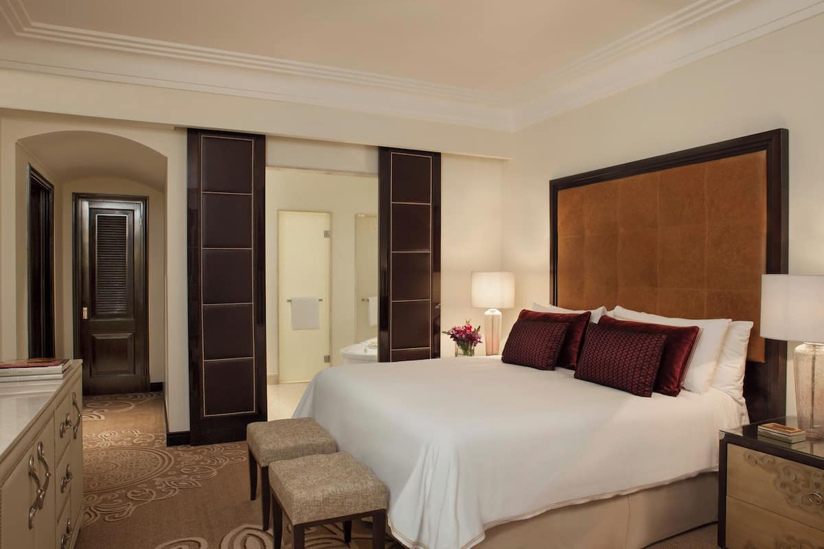Una habitación de hotel con una cama grande, una mesita de noche, un aparador y un banco.