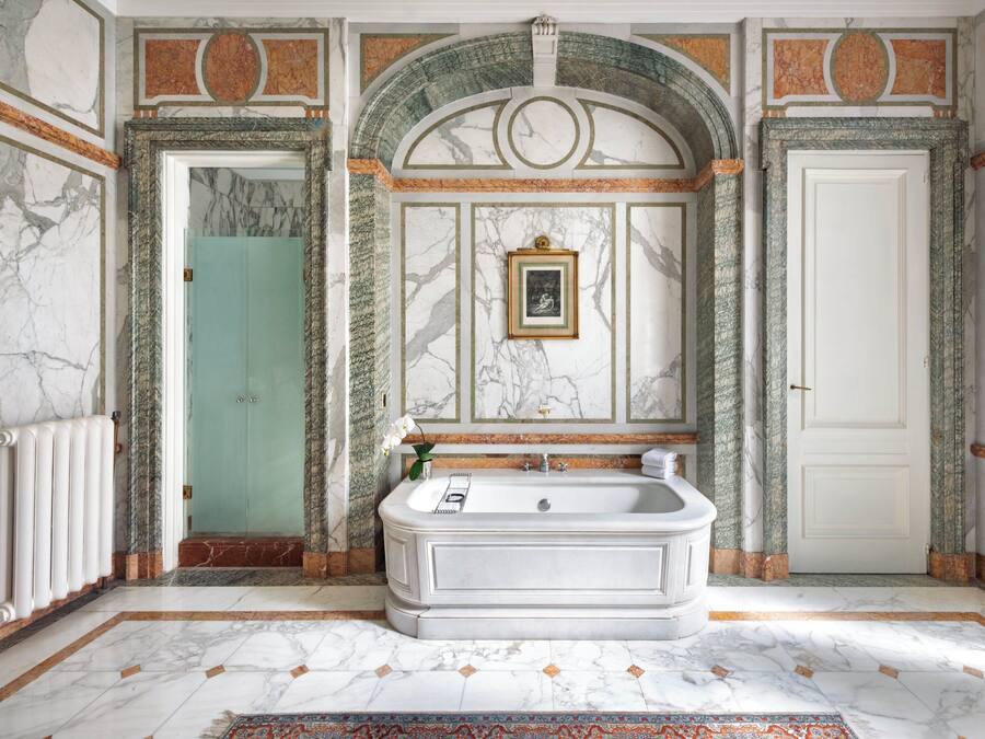Un baño lujoso con una bañera independiente, paredes de mármol y un arco decorativo.