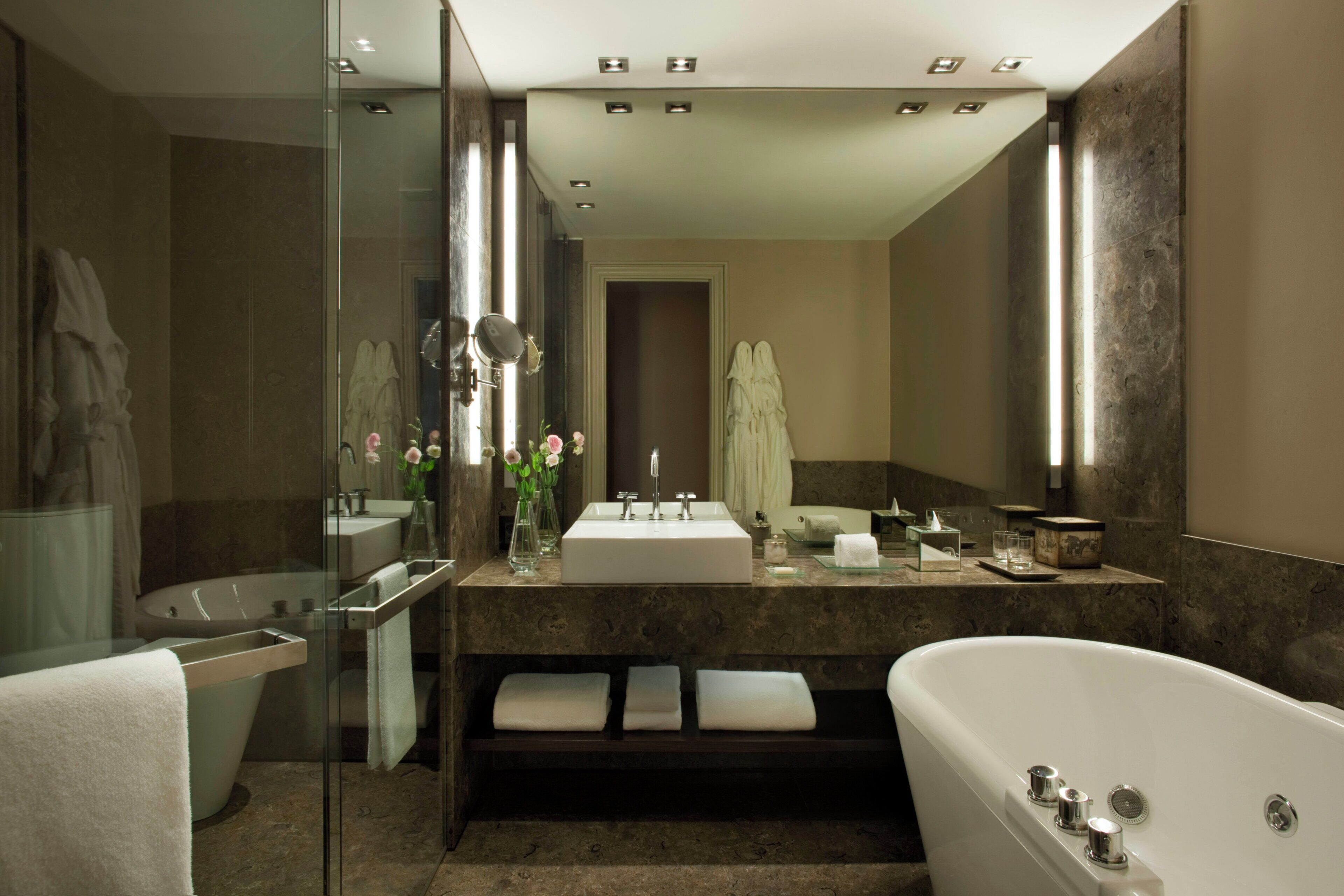 A modern bathroom with a freestanding bathtub, a glass-enclosed shower, a large mirror, and a vanity with a sink and countertop.