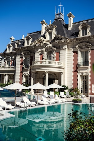 A large building with a swimming pool, white lounge chairs, and umbrellas.