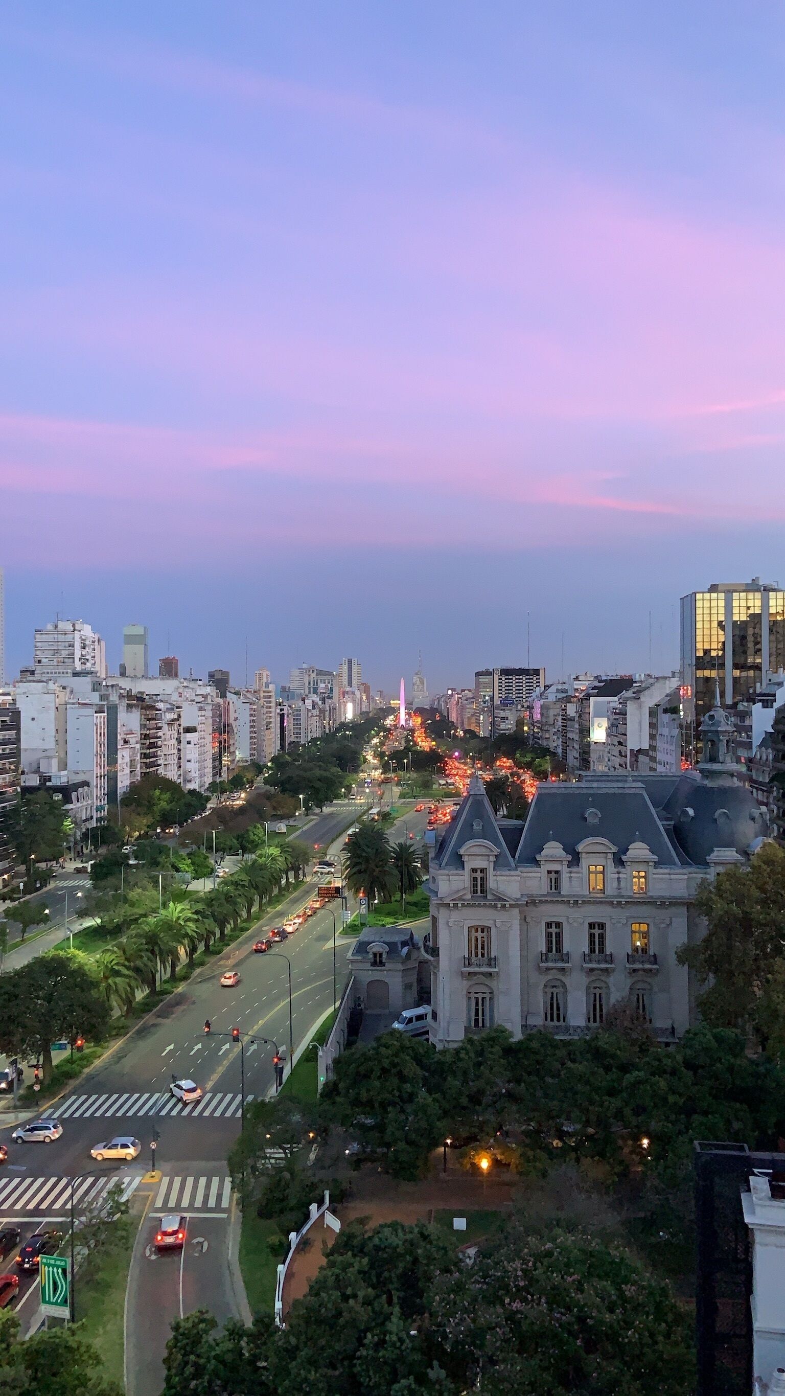A cityscape at dusk with modern buildings, a prominent pink monument, and a well-lit historic building.