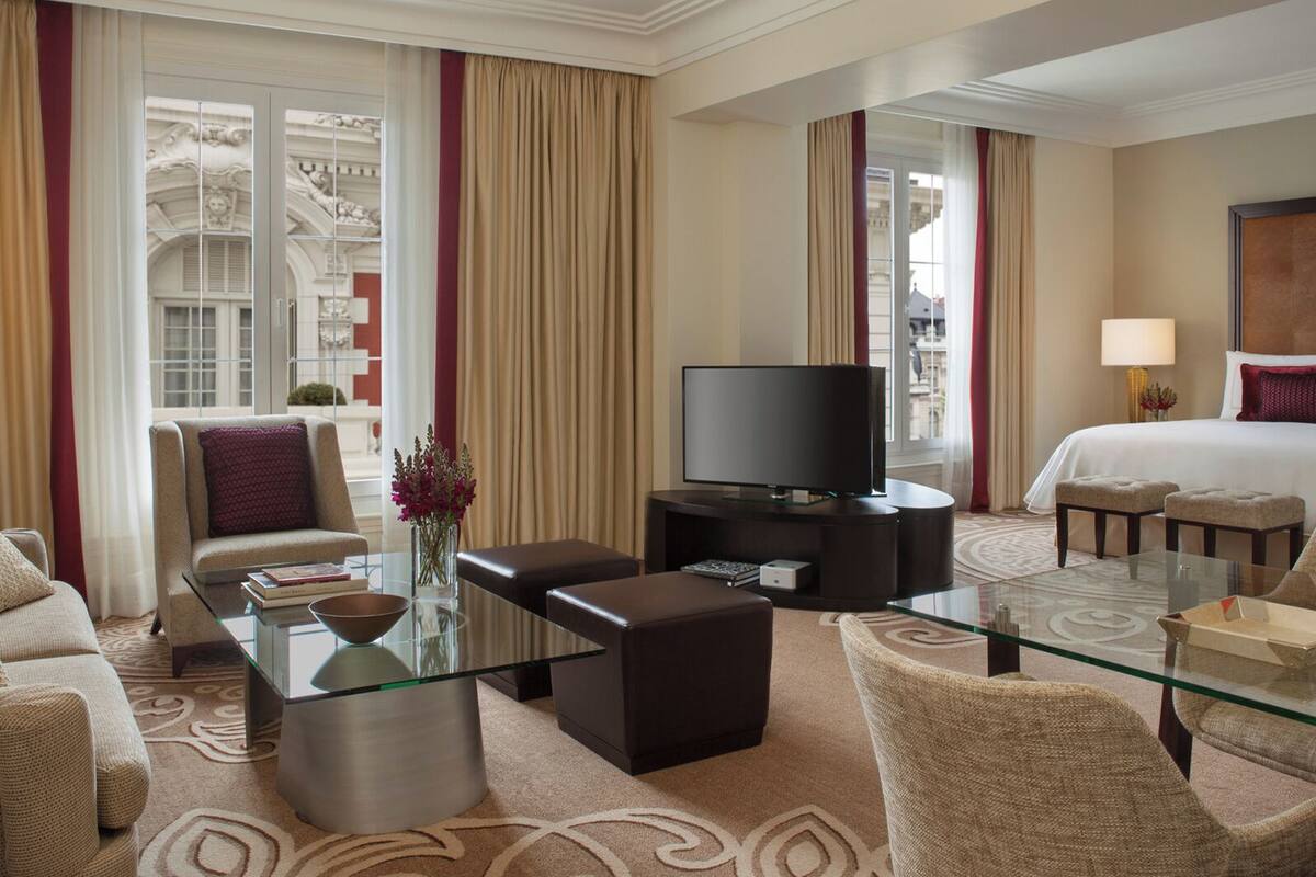 Habitación de hotel con una mesa de centro de vidrio, un sofá, un televisor, una cama y vistas a la ciudad.