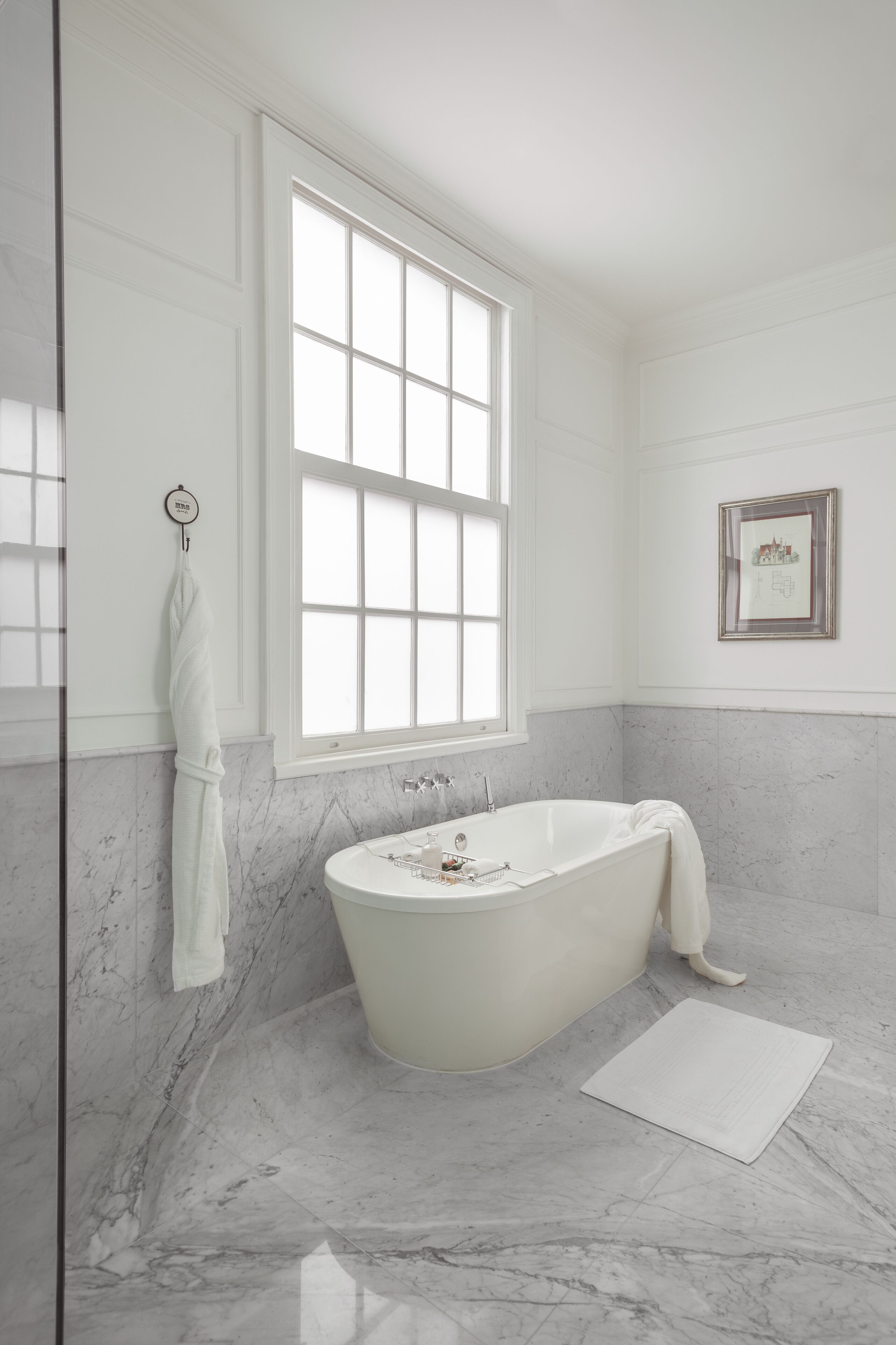 A bathroom with a freestanding bathtub, a large window, and marble walls.
