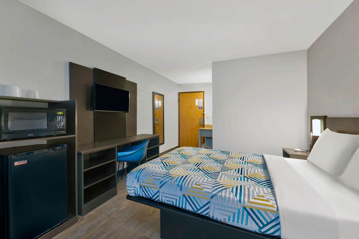 Ein Hotelzimmer mit einem Bett, einem Schreibtisch mit Stuhl, einer Mikrowelle und einem Kühlschrank.
