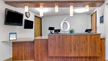 Un mostrador de recepción con detalles de madera, un reloj y el número '6' de gran tamaño en la pared.