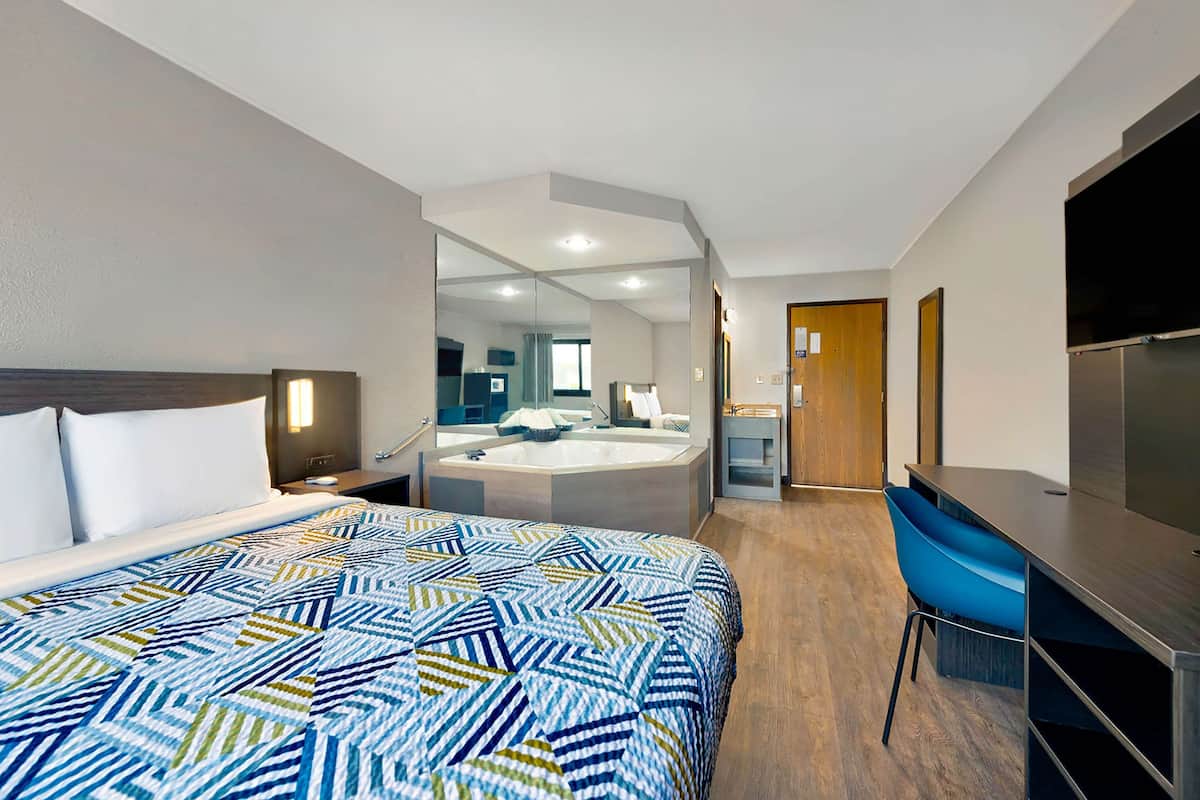 Ein modernes Hotelzimmer mit einem großen Bett, einem Schreibtisch, einem Stuhl, einem Badezimmer mit Badewanne und einem Fernseher.