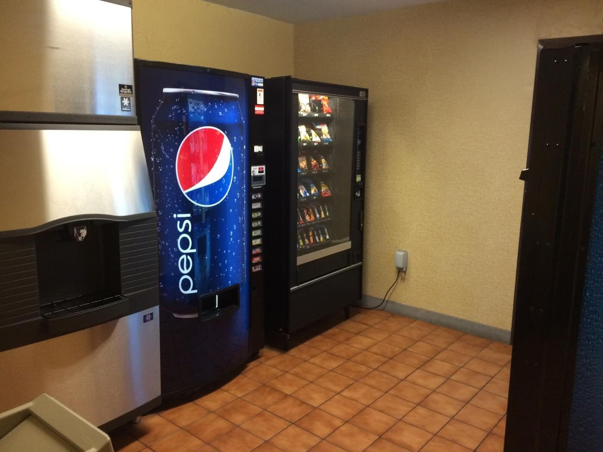 A room with a refrigerator, a Pepsi vending machine, and a snack vending machine.