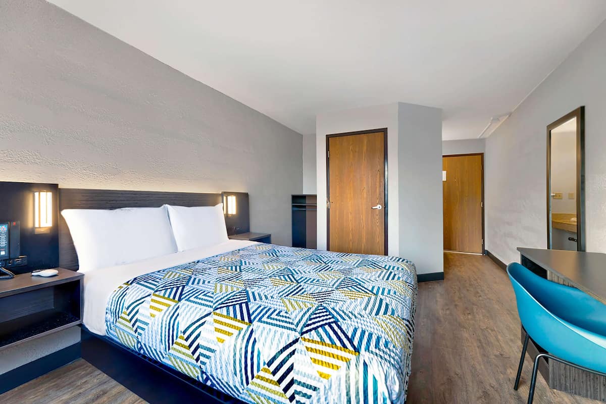 Ein Hotelzimmer mit Bett, Nachttisch, Lampe und Schreibtisch mit Stuhl.