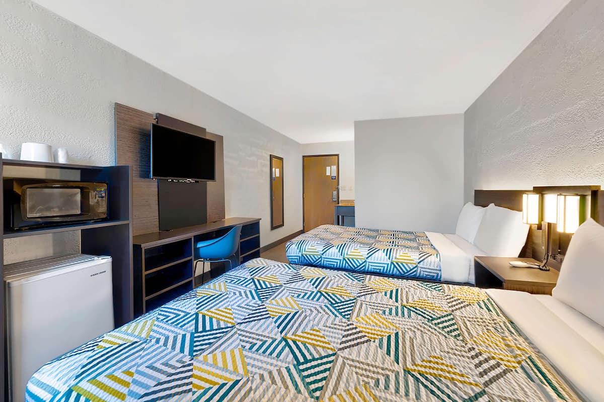 Ein Hotelzimmer mit zwei Betten, einem Fernseher, einem Kühlschrank und einem Schreibtisch mit Stuhl.