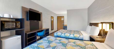 Een hotelkamer met twee bedden, een televisie, een koelkast en een bureau met stoel.