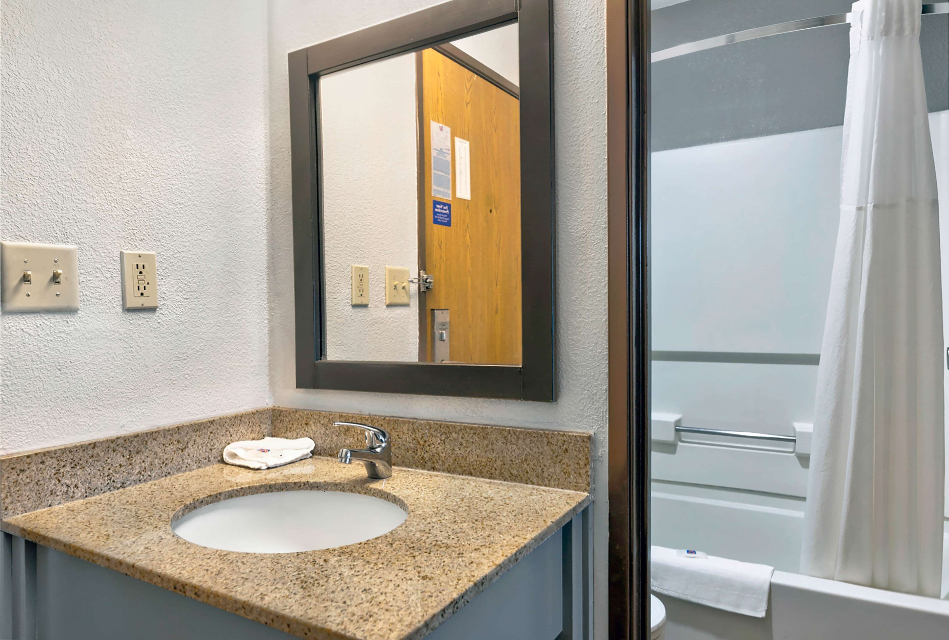 A bathroom with a granite countertop sink, a mirror, and a shower with a white curtain.