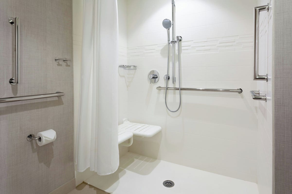 A modern bathroom with a walk-in shower, grab bars, a toilet paper holder, and a showerhead.