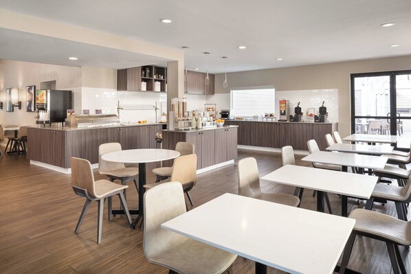 A modern hotel lobby with a central bar, seating area, and a large window providing natural light.