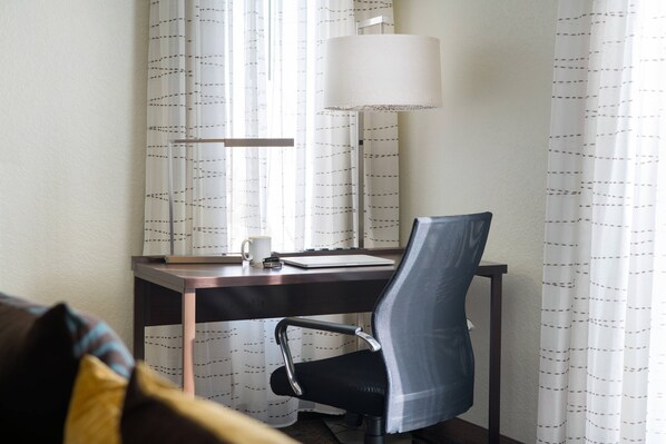 A hotel room with a desk, chair, lamp, and curtains.