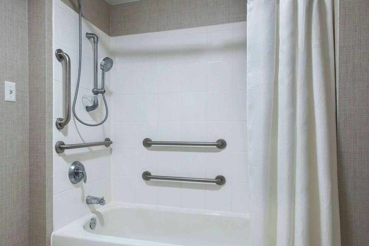 A bathroom with a bathtub, grab bars, and a showerhead.