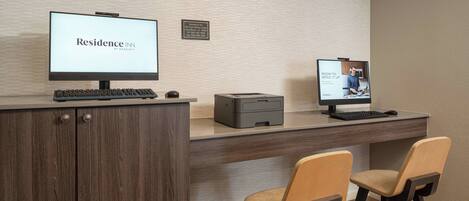 Un mostrador de recepción de hotel con dos monitores de computadora, una impresora y dos sillas.