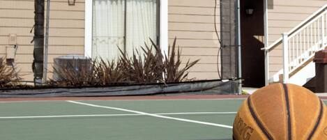 Una canasta de baloncesto, una raqueta de tenis y una pelota de tenis en una cancha.