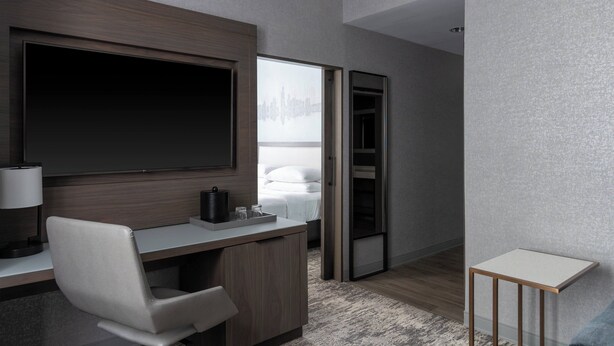 Quarto de hotel moderno com uma televisão de tela plana grande, uma escrivaninha com cadeira, mesa de cabeceira e um closet espaçoso.