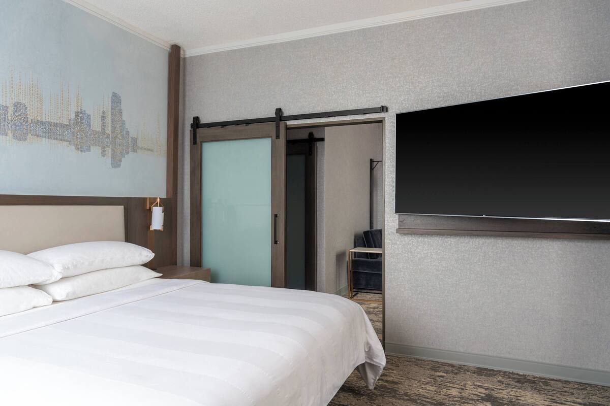 A hotel room with a bed, a sliding door closet, a television, and a cityscape mural on the wall.