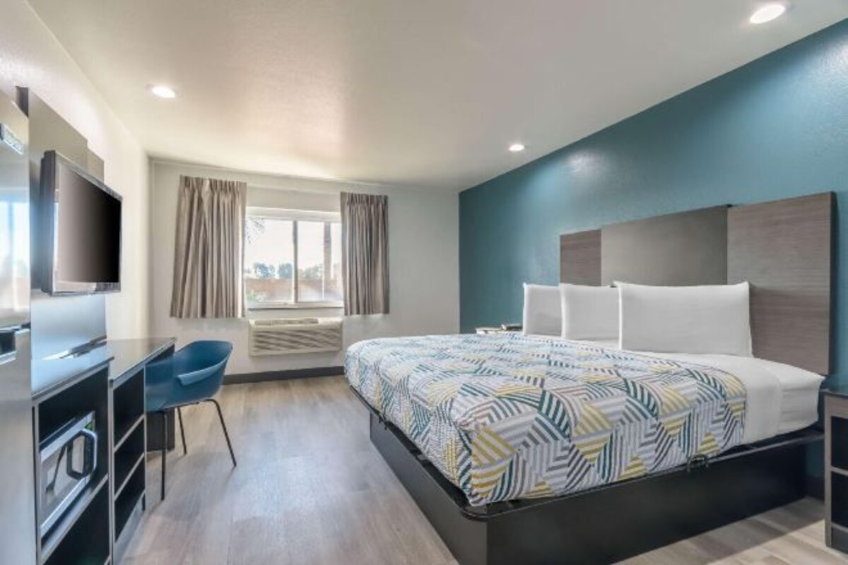 A modern hotel room with a bed, a TV, a desk, and a chair.