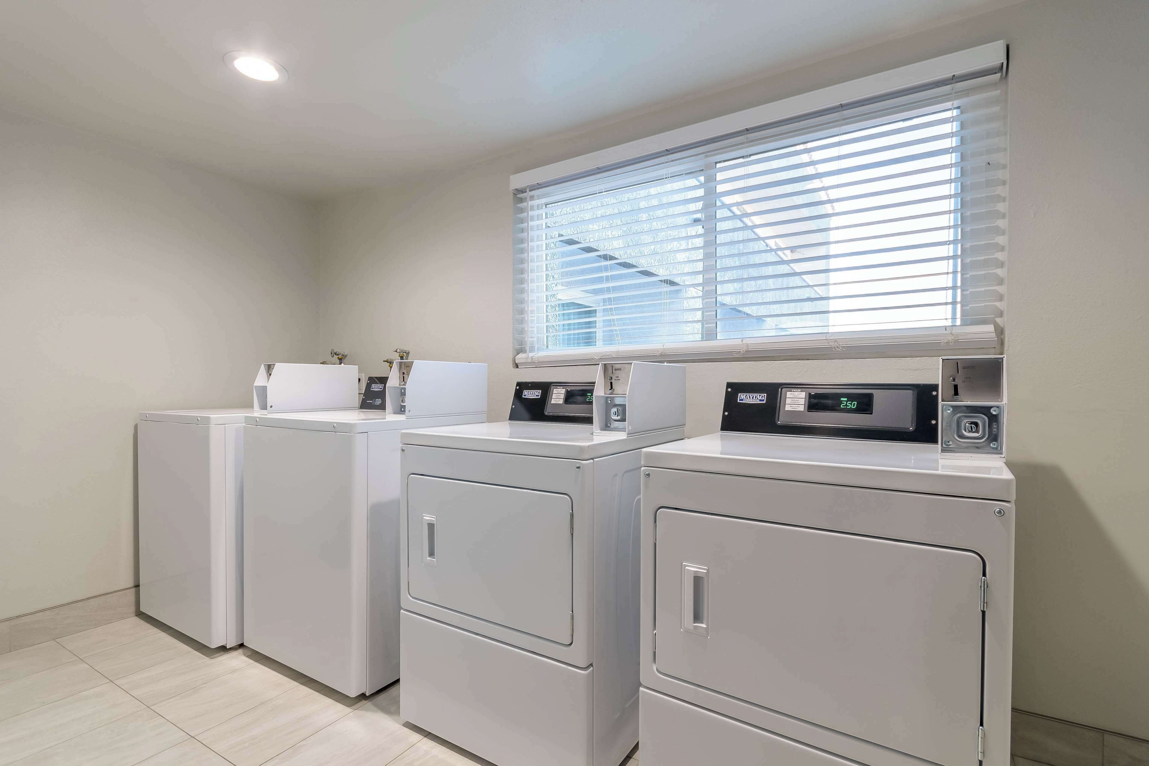 A laundry area with three stacked washers and dryers, a window with blinds, and a ceiling light.