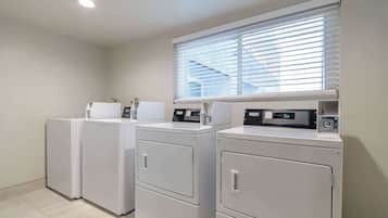 A laundry area with three stacked washers and dryers, a window with blinds, and a ceiling light.