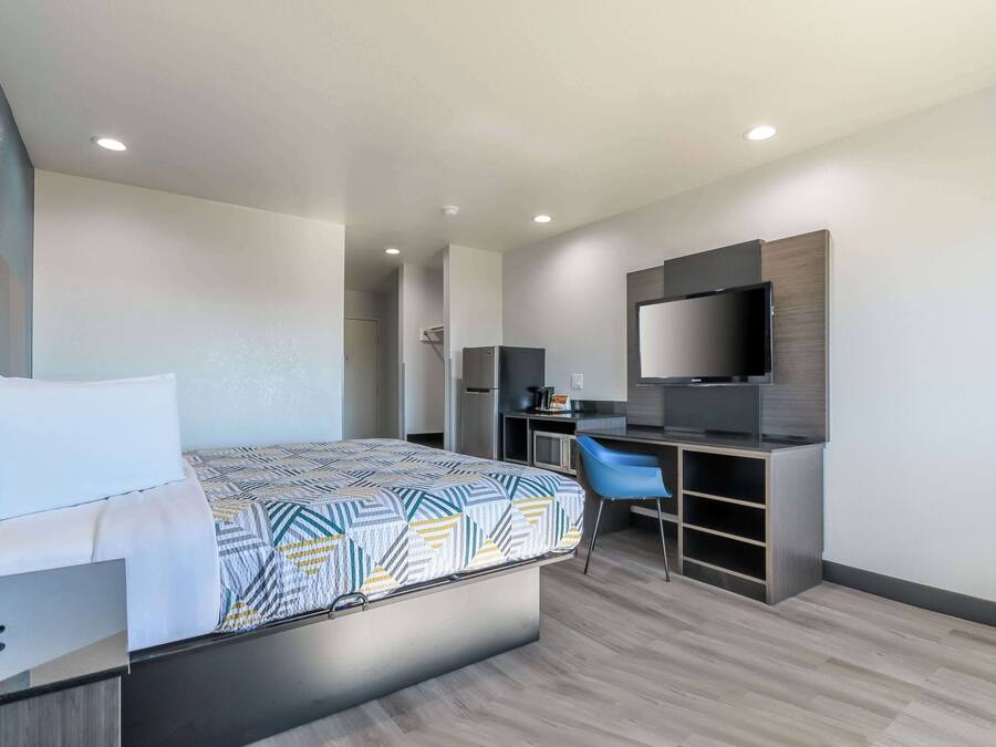 Una habitación de hotel moderna con cama, escritorio, silla y televisor de pantalla plana.