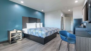 A modern hotel room with a bed, a small desk, a chair, and a kitchenette. - Studio 6 Suites Perris, CA (Perris)