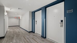 A hallway with a wooden floor, white doors, and a blue accent wall. - Studio 6 Suites Perris, CA (Perris)