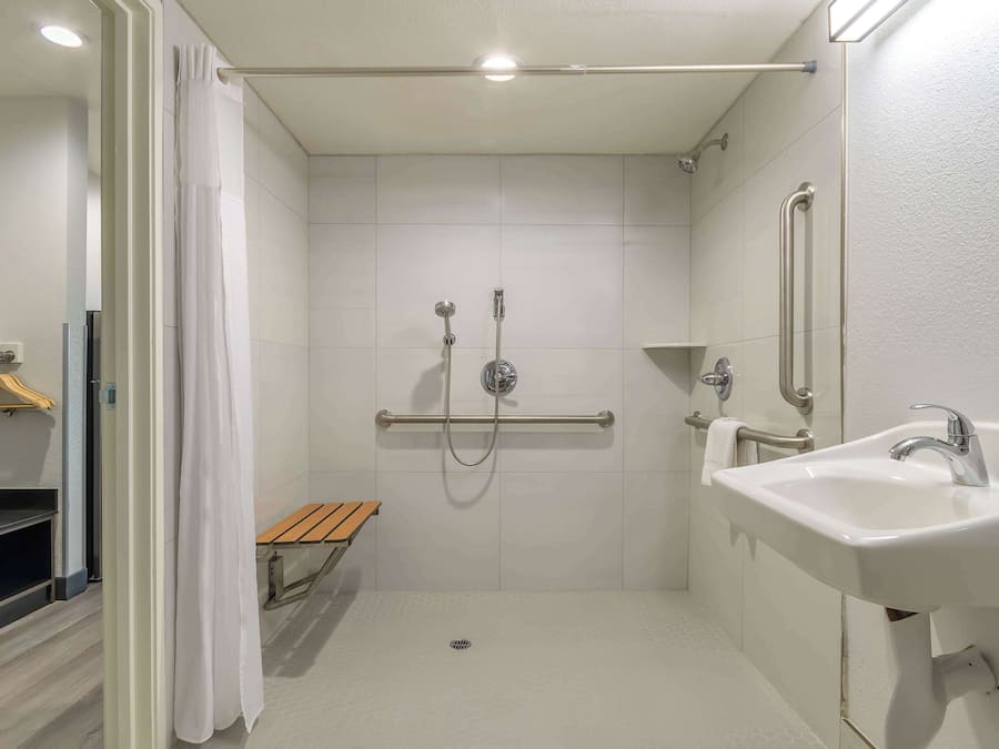 A modern bathroom with a shower, grab bars, a bench, and a sink.