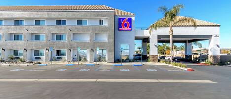 A 6th Street Suites hotel with a parking lot, multiple parking spaces, and a building facade with a blue sign.